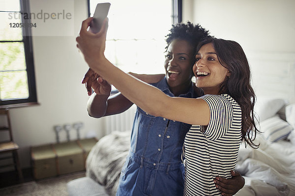 Lächelndes lesbisches Paar  das sich umarmt  Selfie mit Fotohandy im Schlafzimmer.