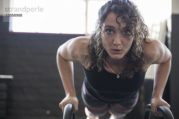 Porträt entschlossene junge Frau beim Liegestütz mit Ausrüstung im Fitnessstudio