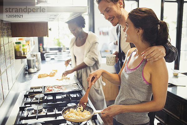 Junges Paar beim Kochen von Rühreiern auf dem Herd in der Küche