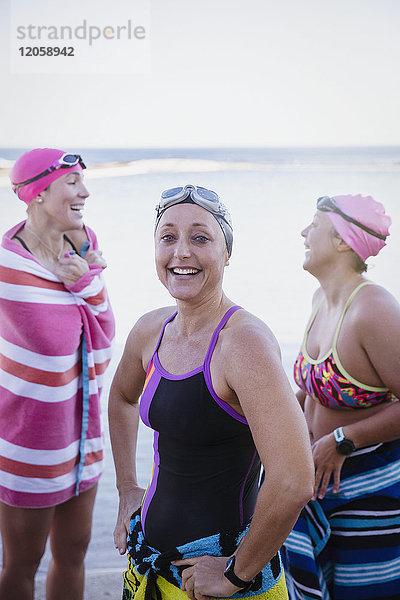 Portrait lächelnde  selbstbewusste Schwimmerinnen  die mit Handtüchern am Meer trocknen.