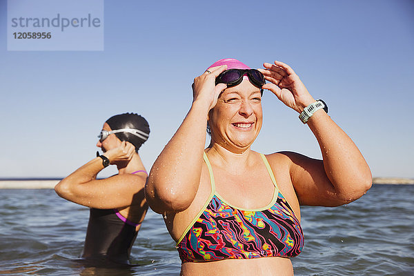 Lächelnde  fröhliche Schwimmerin  die eine Schwimmbrille im sonnigen Meer anpasst.