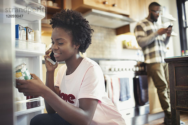 Frau spricht auf Smartphone  liest Etikett auf Glas im Kühlschrank in der Küche