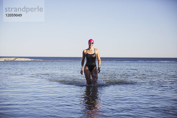 Porträt einer Schwimmerin im offenen Wasser  die im sonnigen Meer spazieren geht.