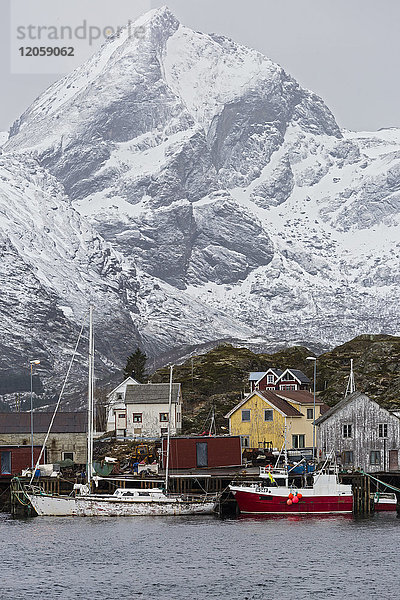 Fischerdorf und Boote am Wasser unter verschneiten  zerklüfteten Bergen  Sund  Lofoten  Norwegen