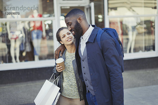 Zärtliches junges Paar mit Kaffee und Einkaufstasche vor dem Schaufenster
