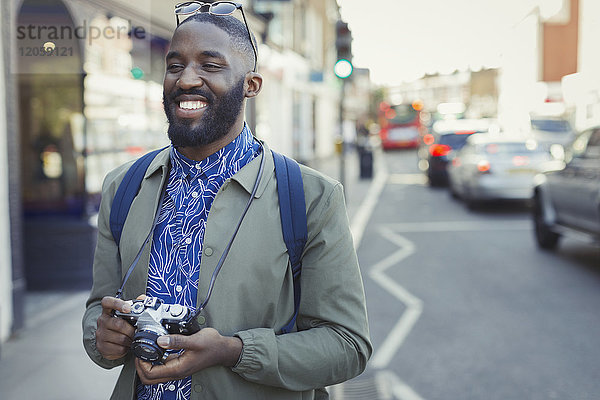 Lächelnder junger männlicher Tourist mit Kamera auf städtischer Straße