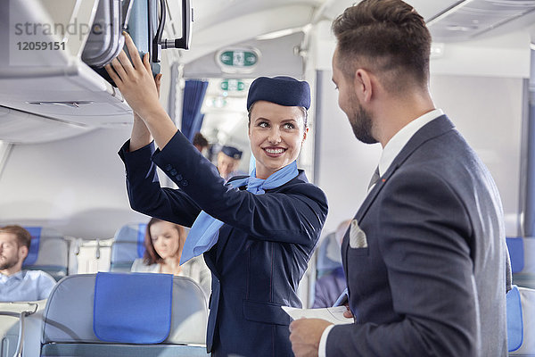 Flugbegleiter hilft Geschäftsmann mit Gepäck im Flugzeug