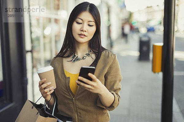 Junge Frau mit Kaffee SMS mit Handy auf städtischem Bürgersteig