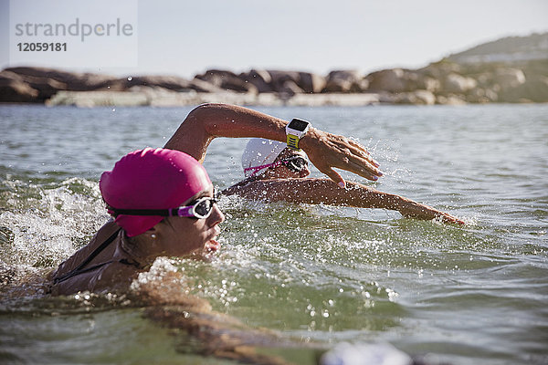 Entschlossene Schwimmerin mit smarter Uhr im sonnigen Meer schwimmend