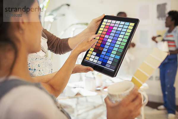 Junge Frau trinkt Kaffee und sieht sich digitale Farbmuster auf einem digitalen Tablett an.