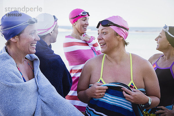 Weibliche Schwimmerinnen reden und trocknen mit Handtüchern am Strand.