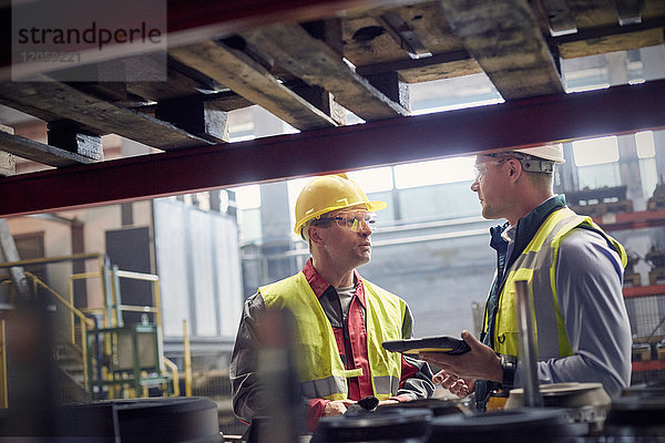 Stahlarbeiter mit digitalem Tablett sprechen im Stahlwerk