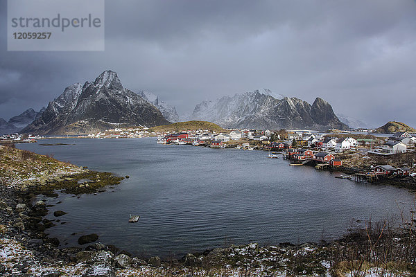 Fischerdorf am Wasser unter verschneiten  zerklüfteten Bergen  Reine  Lofoten  Norwegen