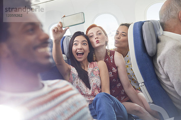 Verspielte junge Freunde mit Fotohandy  die Selfie im Flugzeug mitnehmen.