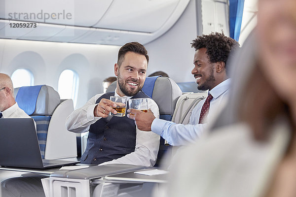 Geschäftsleute rösten Whiskygläser in der ersten Klasse im Flugzeug.