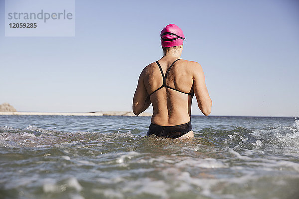 Weibliche Freiwasserschwimmerin beim Waten in der sonnigen Meeresbrandung