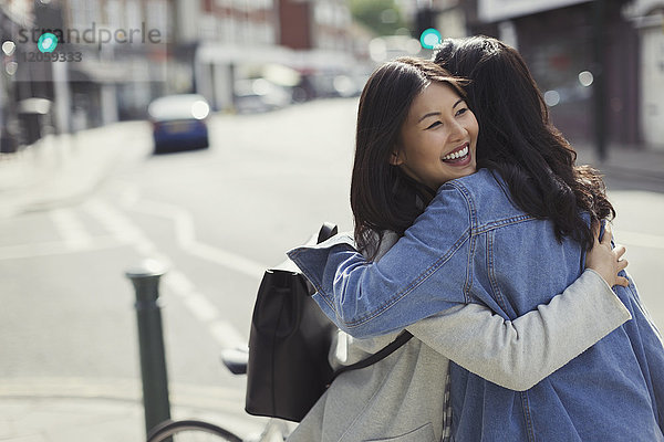 Lächelnde  liebevolle Freundinnen  die sich auf einer sonnigen  städtischen Straße umarmen.