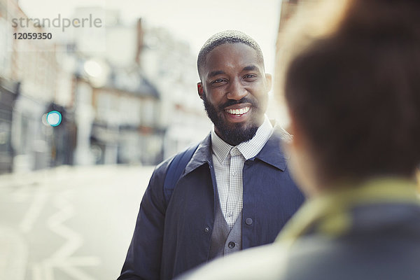 Lächelnder Geschäftsmann im Gespräch mit einem Freund auf einer sonnigen Stadtstraße