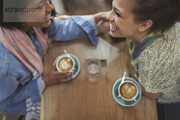 Junge liebevolle Freundinnen trinken Kaffee und lachen im Cafe