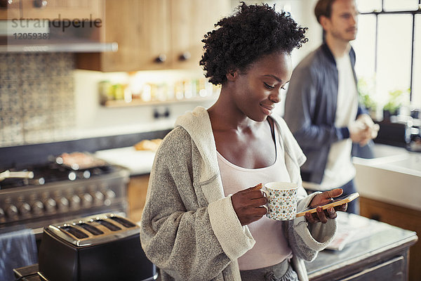 Frau trinkt Kaffee  SMS mit Smartphone in der Küche