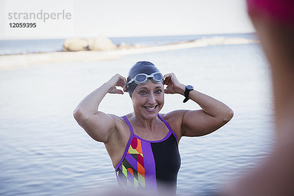 Lächelnde Schwimmerin  die Schwimmkappe und Schutzbrille im Meer anpasst