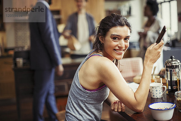 Portrait lächelnde junge Frau SMS mit Smartphone am Frühstückstisch