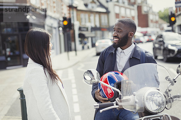 Lächelnder junger Geschäftsmann auf dem Motorroller im Gespräch mit einem Freund auf der Stadtstraße
