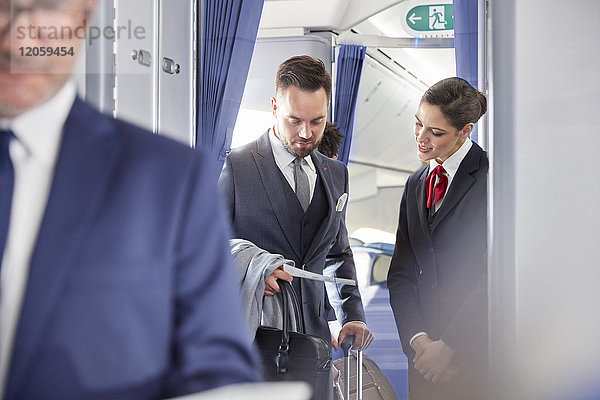 Flugbegleiterin hilft Geschäftsmann mit Bordkarte im Flugzeug