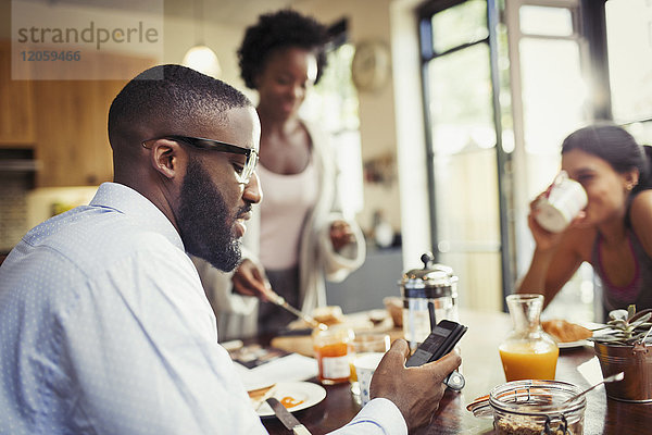Mann trinkt Kaffee und SMS mit Smartphone am Frühstückstisch