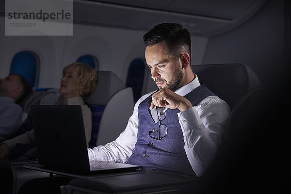 Seriöser Geschäftsmann bei der Arbeit am Laptop im Übernacht-Flugzeug