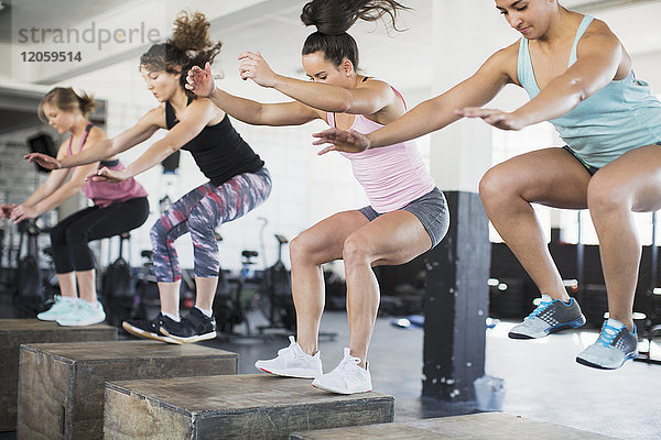 Entschlossene Frauen  die Sprunghocken auf Boxen in der Übungsklasse machen.