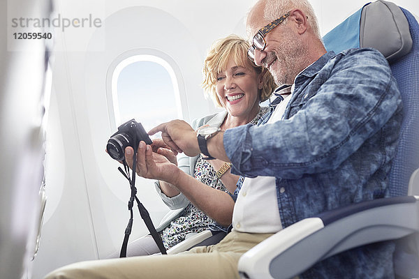 Älteres Ehepaar beim Betrachten von Fotos auf der Digitalkamera im Flugzeug