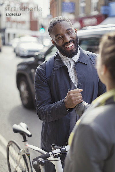 Lächelnder Geschäftsmann mit einem Fahrrad  das der Frau auf der Straße die Hand schüttelt.