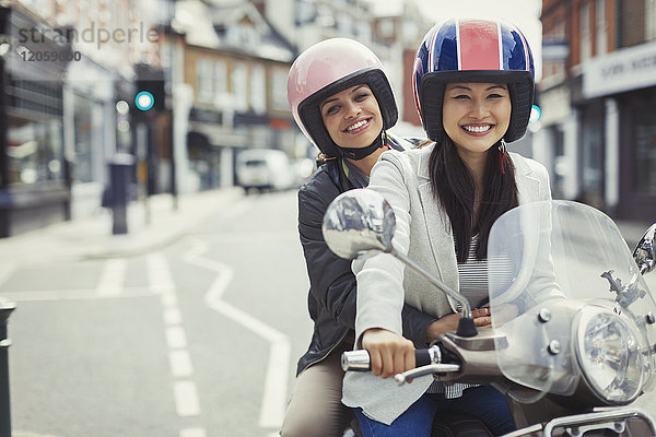 Lächelnde junge Frauen  die Helme tragen  Motorroller fahren in der Stadt.