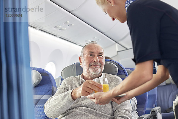 Flugbegleiterin  die dem Mann im Flugzeug Orangensaft serviert.