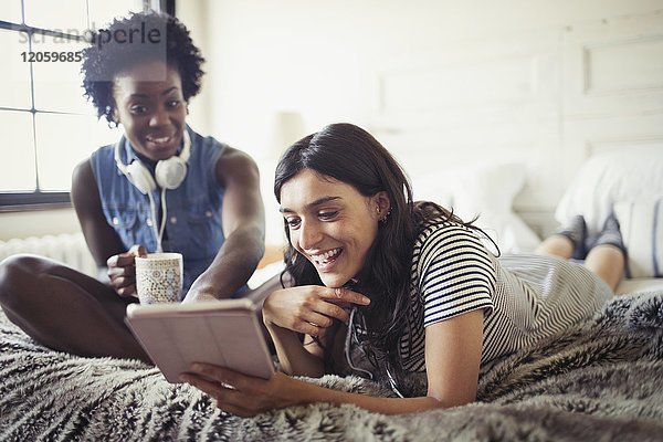 Lächelnde Frauen trinken Kaffee und benutzen Tablet PCn auf dem Bett