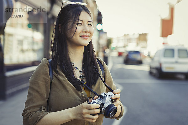 Lächelnde junge Touristenfotografin mit Kamera auf der Stadtstraße