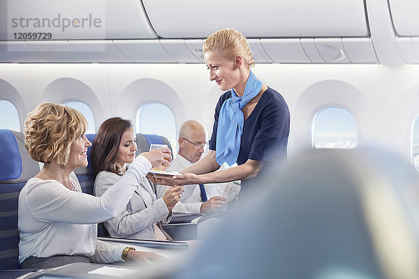 Flugbegleiterin  die der Frau im Flugzeug einen Drink serviert.