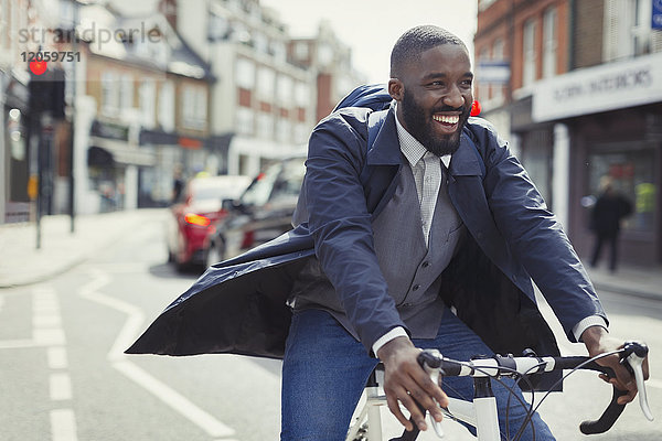 Lächelnder junger Geschäftsmann beim Pendeln  Fahrradfahren auf sonniger Stadtstraße