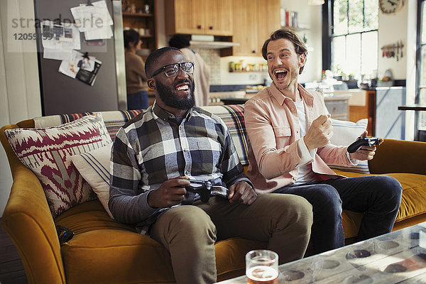 Lachende Männer Freunde spielen Videospiel auf dem Wohnzimmersofa