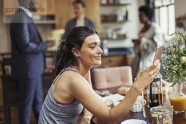 Junge Frau SMS mit Smartphone am Frühstückstisch