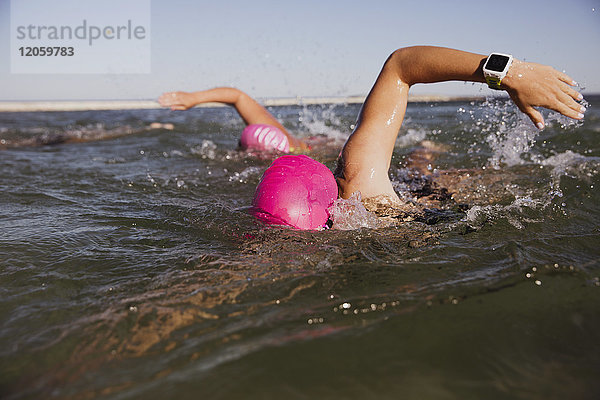 Weibliche Freiwasserschwimmerin mit smarter Uhr im sonnigen Meer schwimmend