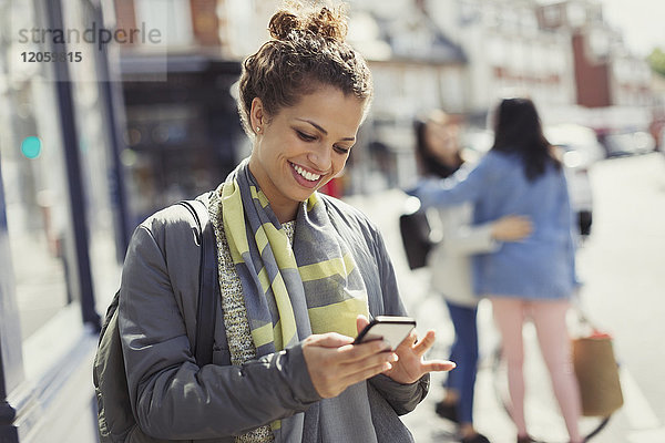 Lächelnde junge Frau beim SMSen mit dem Handy auf der sonnigen Stadtstraße