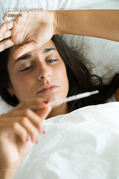 Frau im Bett liegend  Temperaturmessung mit Thermometer