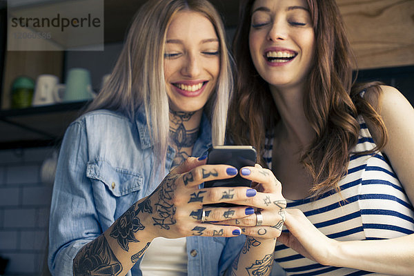 Frauen  die Smartphones anschauen und gemeinsam lachen