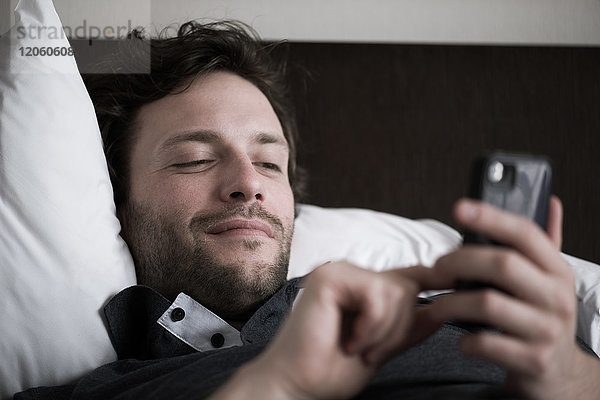 Mann im Bett liegend mit Smartphone