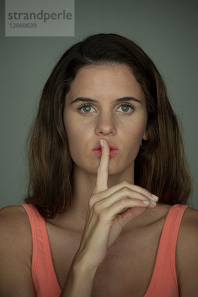 Junge Frau hält den Finger schweigend an den Lippen  Porträt