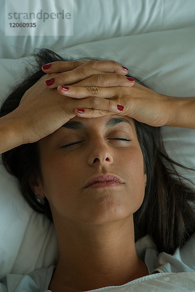 Frau im Bett liegend mit Händen auf der Stirn