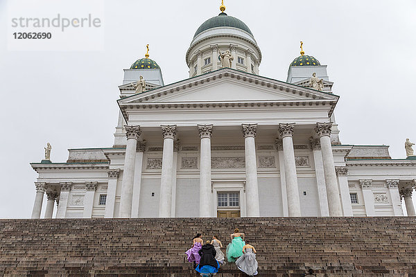 Gruppe von Frauen in farbenfrohen Kleidern  die die Stufen der lutherischen Kathedrale in Helsinki  Finnland  hinaufgehen.