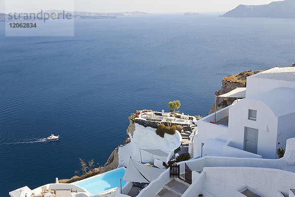 Hochwinkelaufnahme von traditionellen weiß getünchten Häusern und Swimmingpool auf einer griechischen Insel  in der Ferne ein Schiff im Mittelmeer.